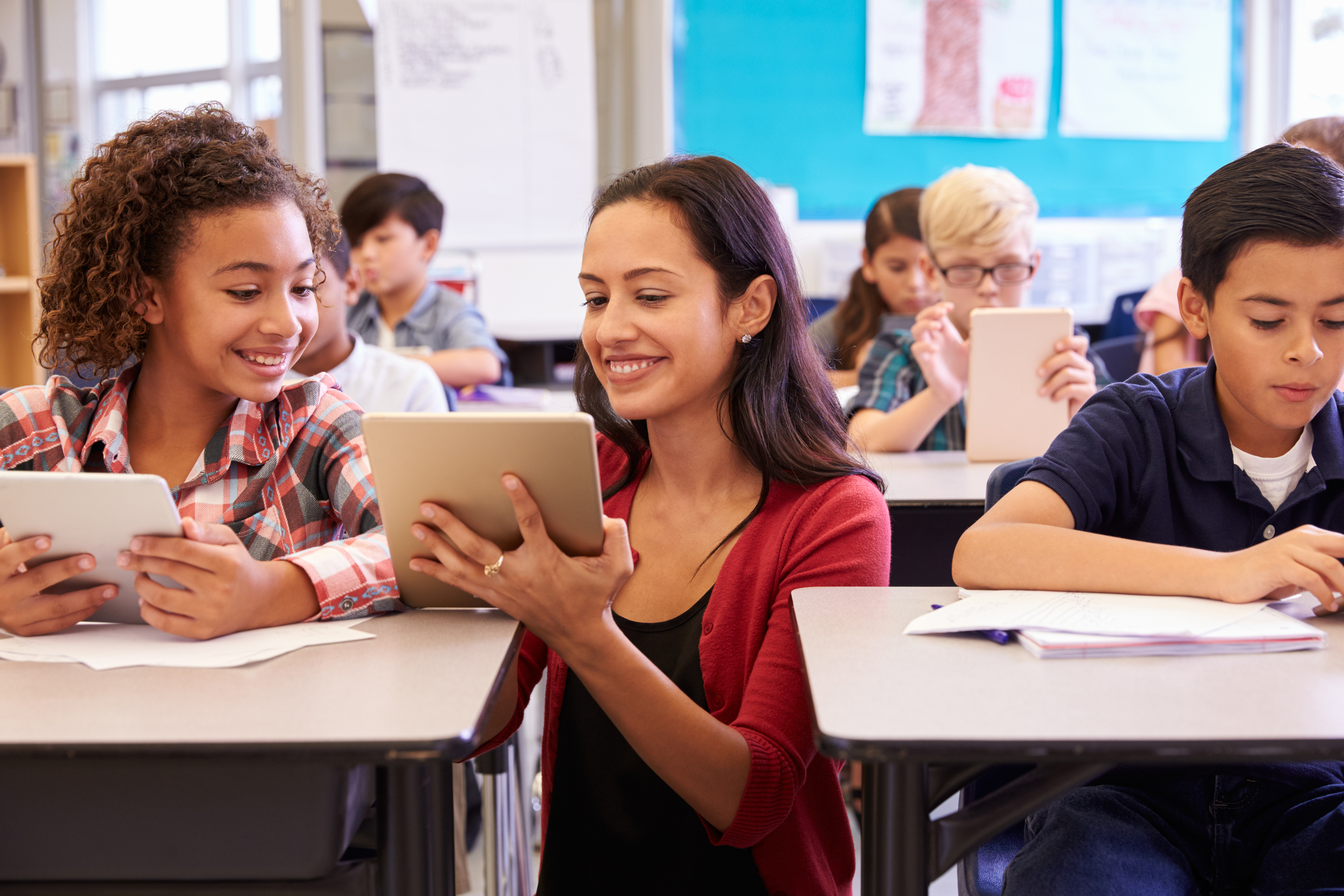 Female teacher helps students with a tablet.