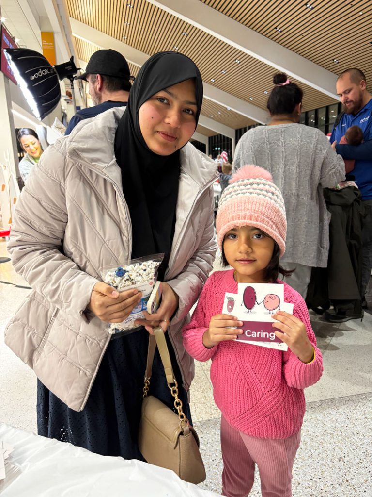Jeni Akter and her daughter, Jarifa, visit the Nurture Nebraska booth at LNK Santa Bash, a community event at the Lincoln Airport on Dec. 5, 2025. Attendees picked up emotion cards, coloring sheets and information on children’s social and emotional development.