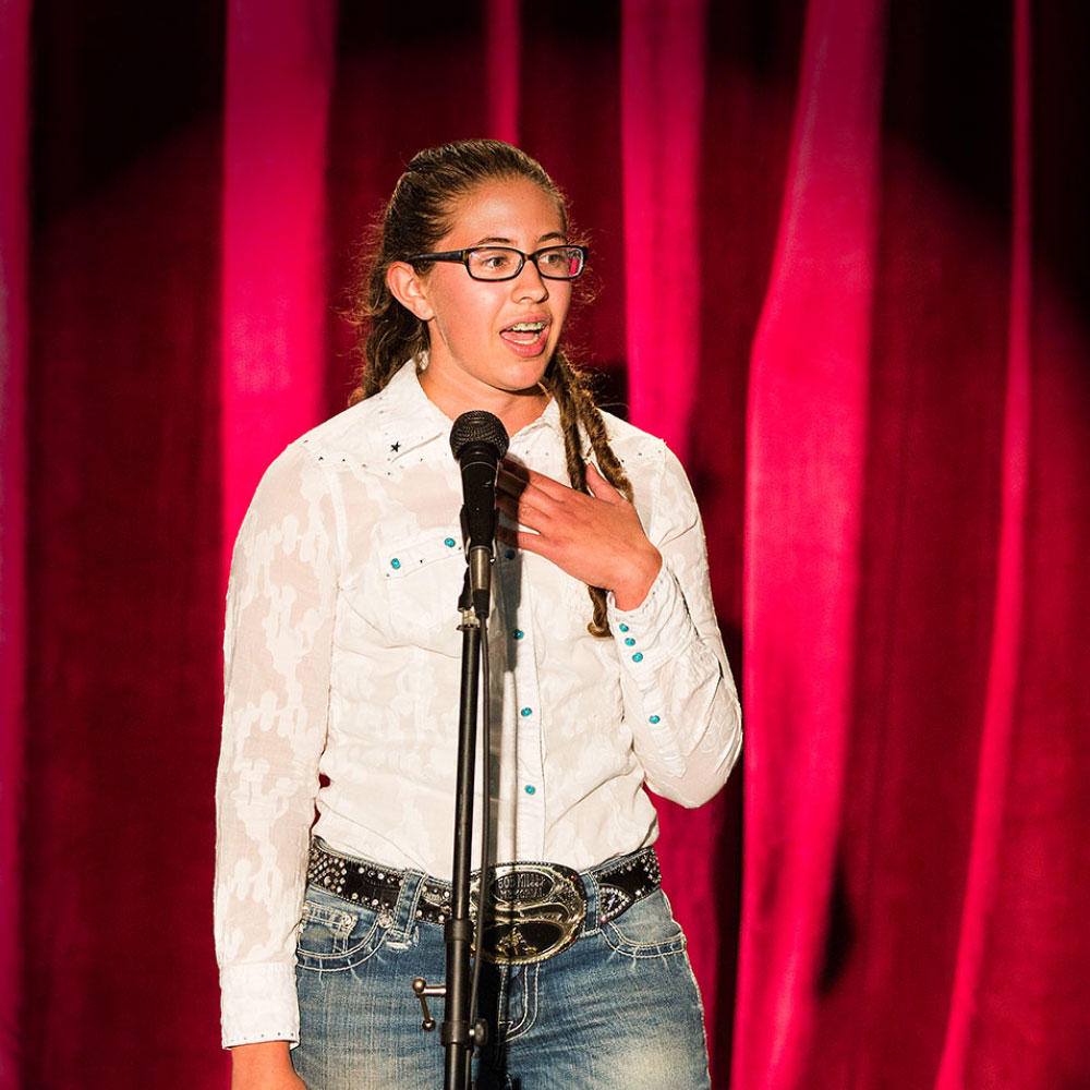 Young woman speaking on stage with spotlight on her.